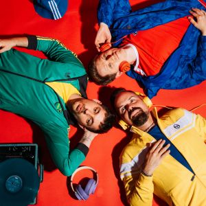 Die Bandmitglieder von Zanadu liegrn auf dem Boden mit bunten Klamotten