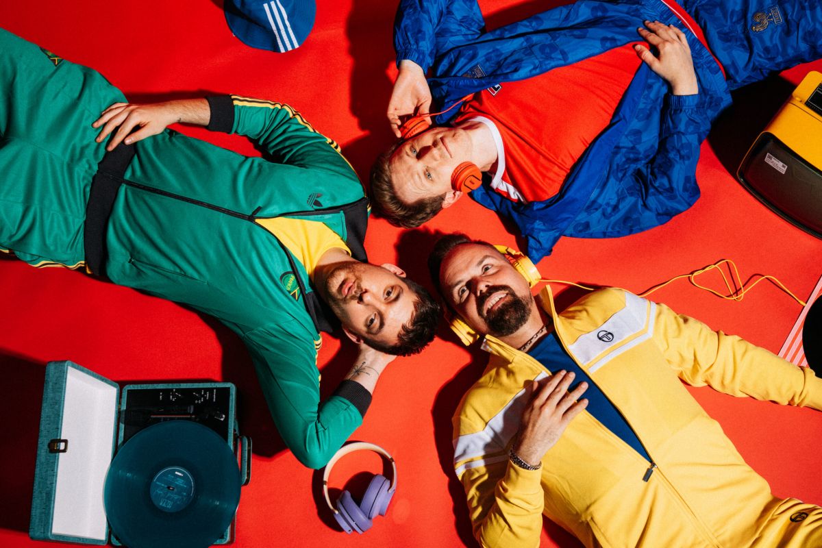 Die Bandmitglieder von Zanadu liegrn auf dem Boden mit bunten Klamotten