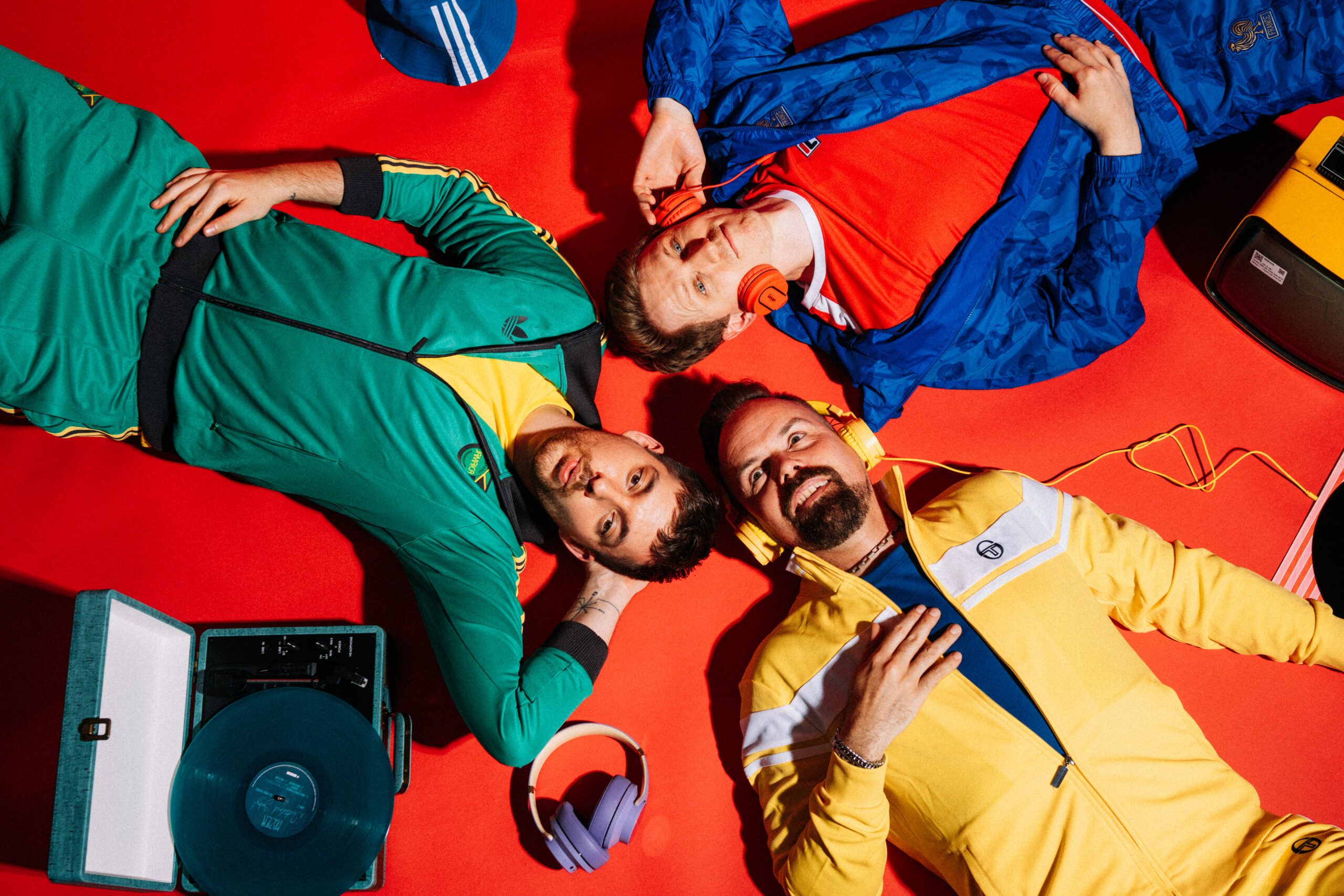 Die Bandmitglieder von Zanadu liegrn auf dem Boden mit bunten Klamotten